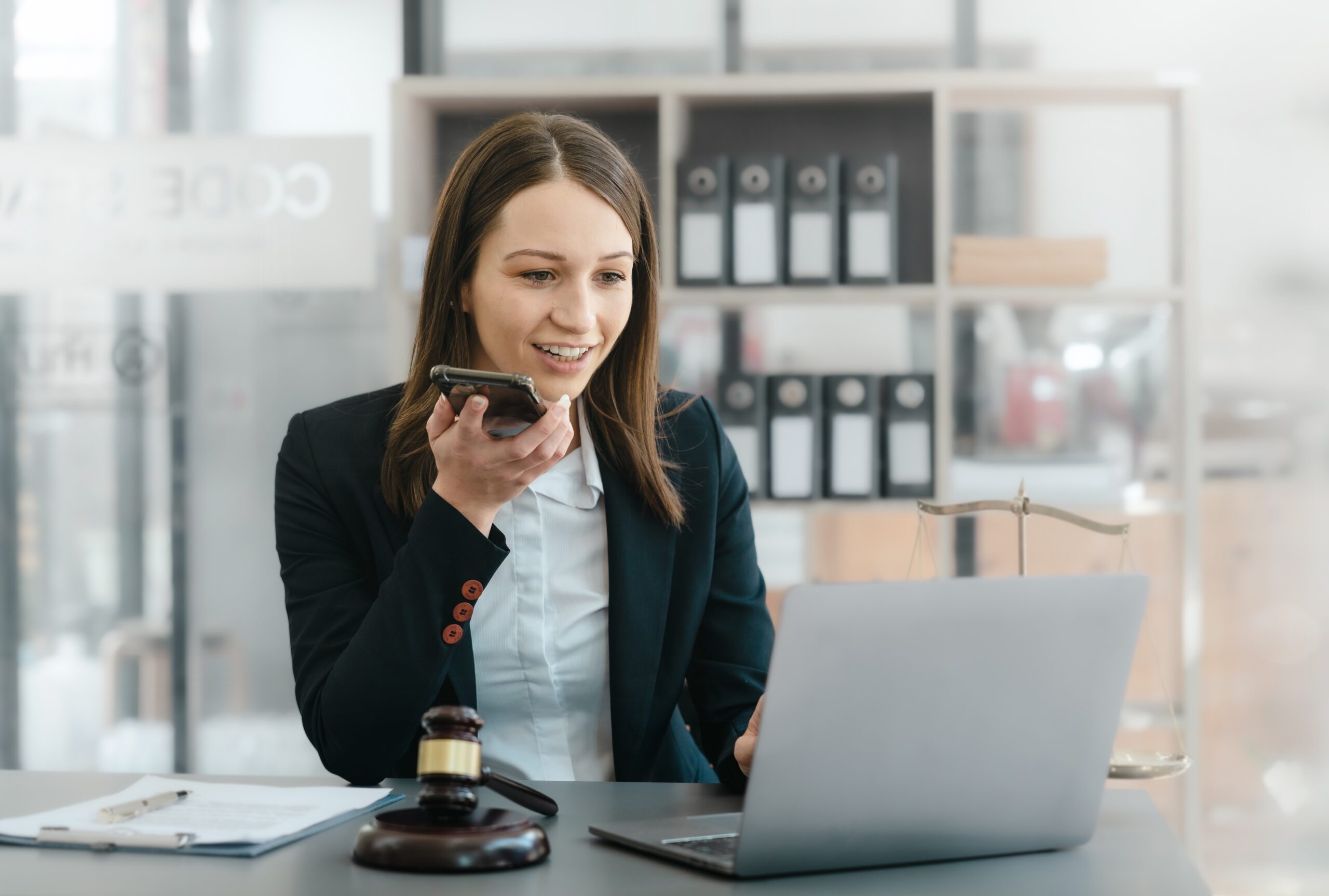 Juriste en droit social travaillant sur un contrat de travail au téléphone devant son ordinateur, avec marteau et balance de justice.